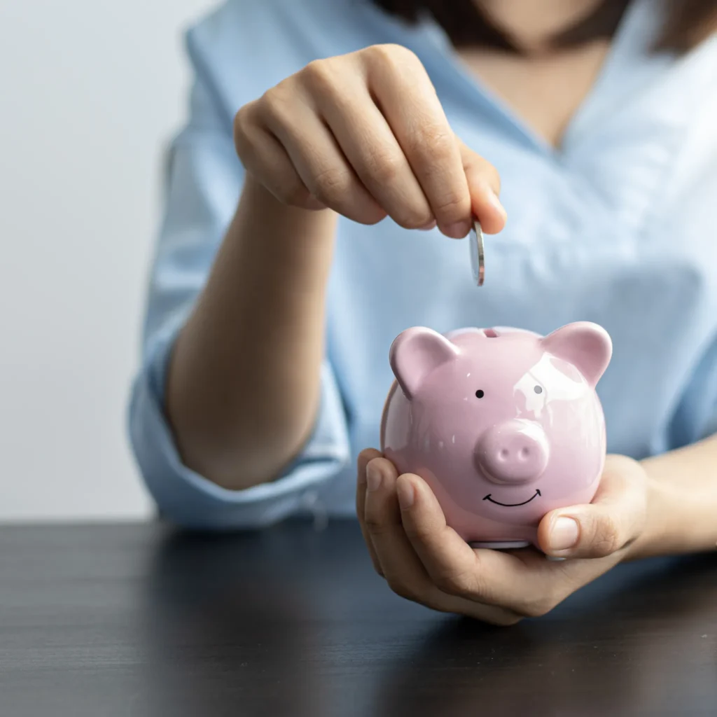Enfoque de una alcancía de cochinito en donde una mano está a punto de ingresar una moneda haciendo una simulación de planes de ahorro.